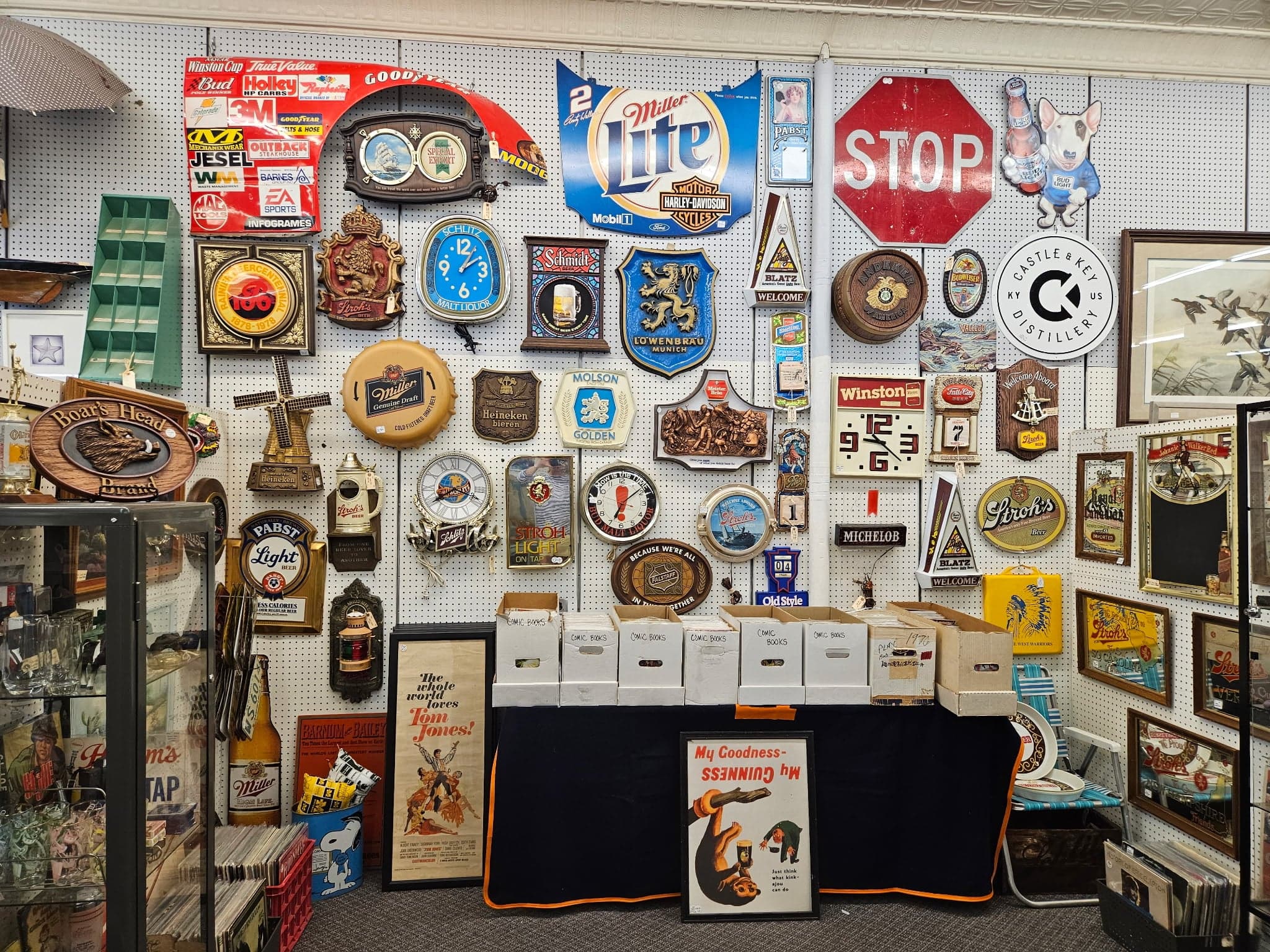 A pegboard wall packed with vintage beer and bar memorabilia, including Miller Lite, Hamm's, and Stroh's signs, an old Stop sign, and beer mirrors.