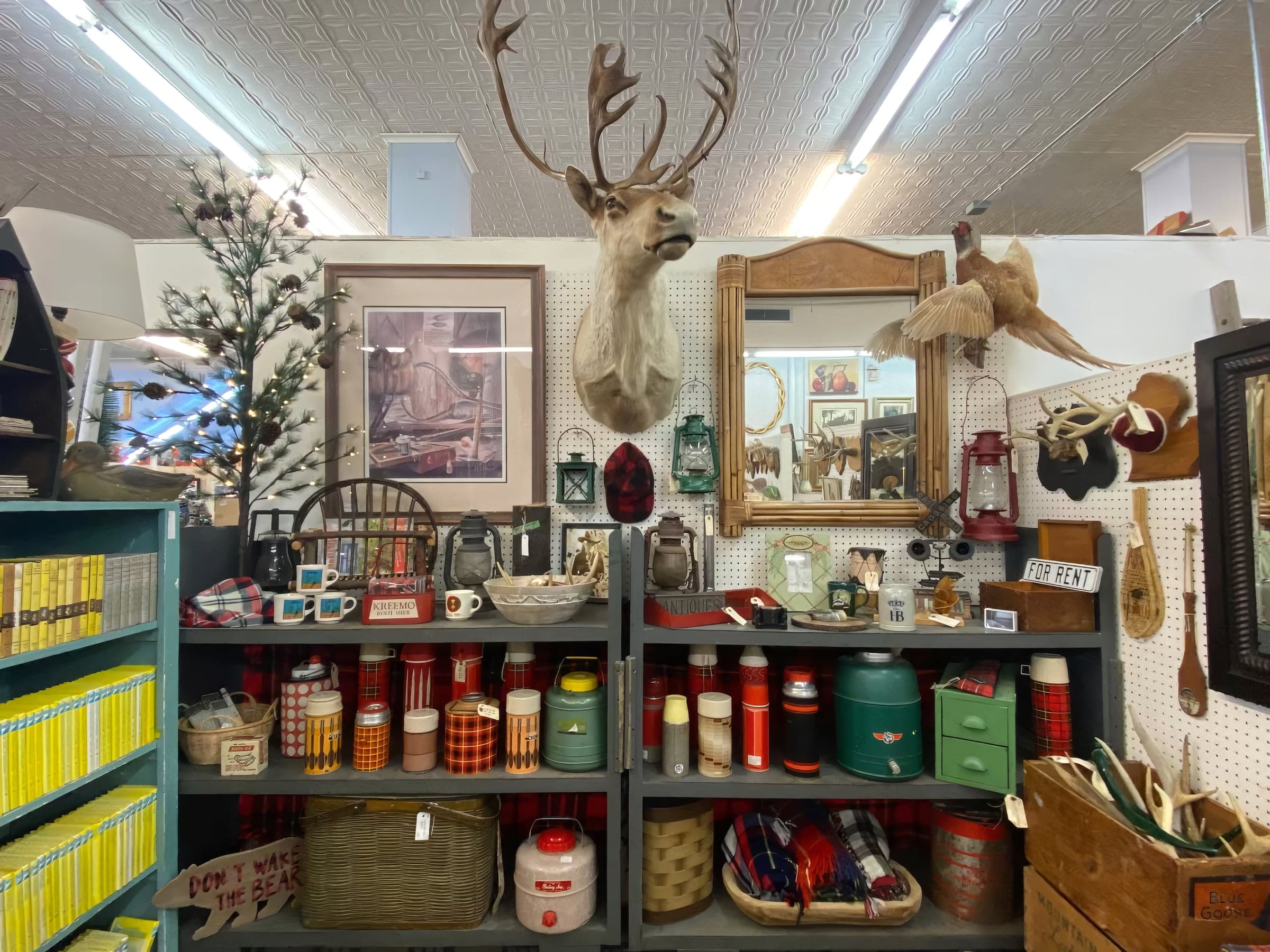 A booth display featuring a mounted deer head and pheasant, hanging vintage lanterns, and shelves of plaid Thermos-brand jugs.
