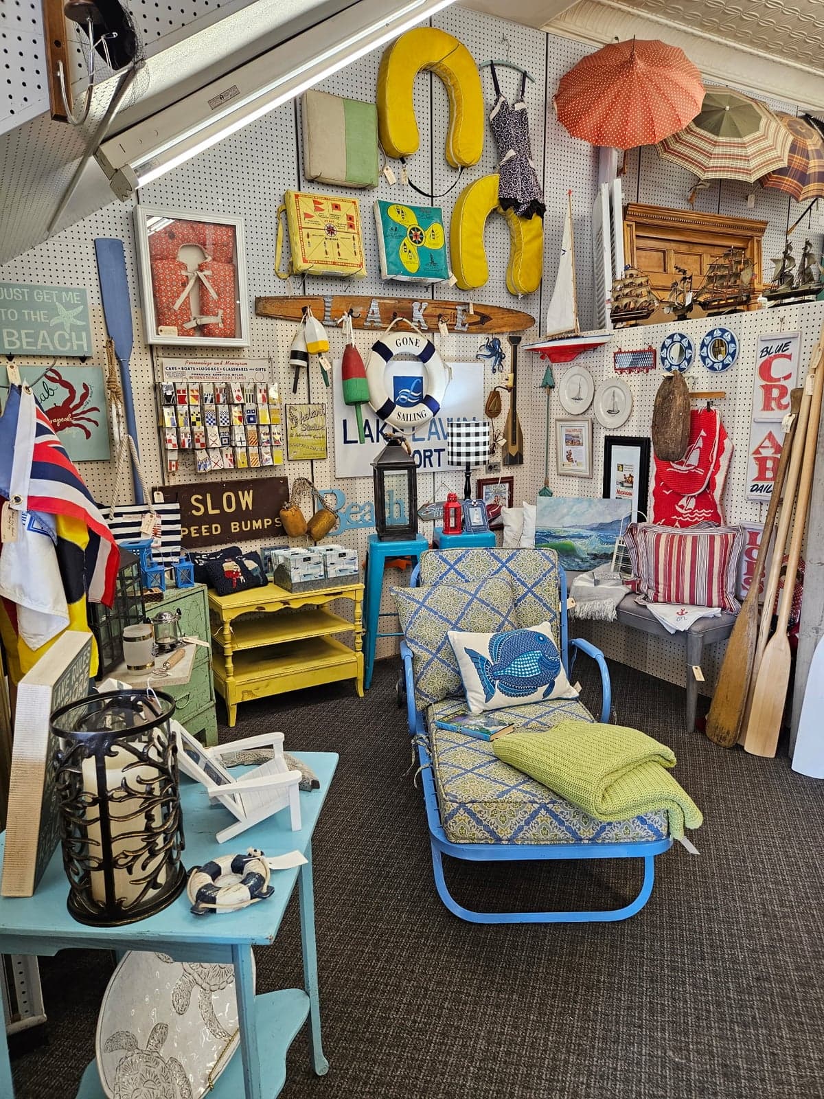 A lake-themed booth display: hanging life ring, painted oars, vintage 'TO THE BEACH' and 'LAKEVIEW' signs, and a blue fish-pillow chaise.